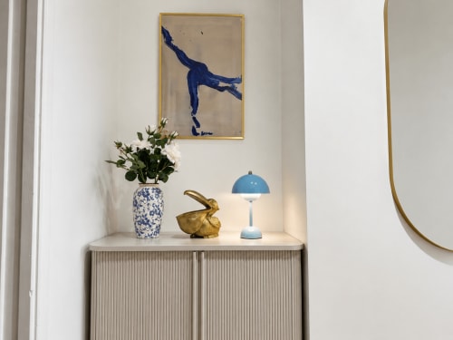Elegante ripiano in moderno appartamento con opera d'arte blu, vaso bianco con fiori, coniglio in ottone e lampada blu con vista sul Pantheon romano