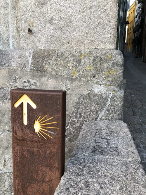 Símbolo de concha de marcação em poste marrom indicando a rota do Camino de Santiago no histórico bairro da Ribeira no Porto