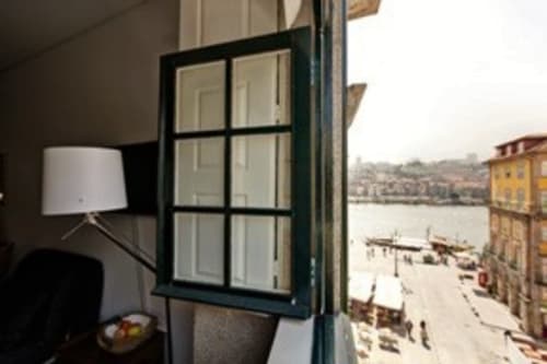Estúdio PortoSense Ribeira no Porto com vista do rio através de janela verde aberta, luminária e paisagem urbano à beira-rio
