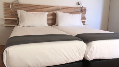 Quarto moderno da PortoSense Ribeira Duplex no Porto com roupa de cama branca, passadeira cinzenta e cabeceira de madeira
