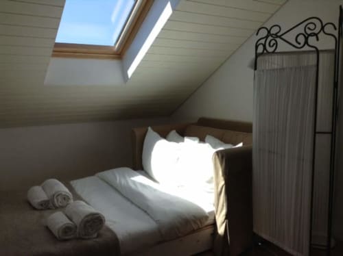 Quarto luminoso sob o telhado no PortoSense Ribeira Duplex no Porto com claraboia, cama de madeira, toalhas enroladas e cortina decorativa