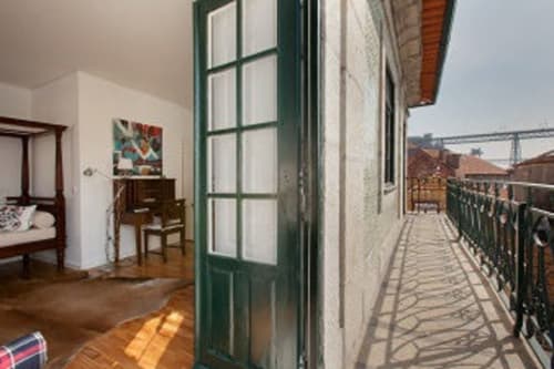 Varanda do duplex PortoSense Ribeira com vista para o rio, portas verdes, assoalho em madeira e ponte do Porto ao longe