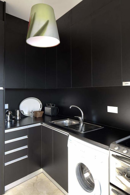 Cozinha preta moderna com pia de aço inoxidável, luminária pendente e máquina de lavar no apartamento duplex PortoSense Ribeira