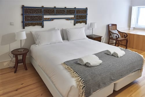 Quarto espaçoso no PortoSense Almada no Porto com roupa de cama branca, cabeceira decorativa, móveis de madeira e toalhas enroladas