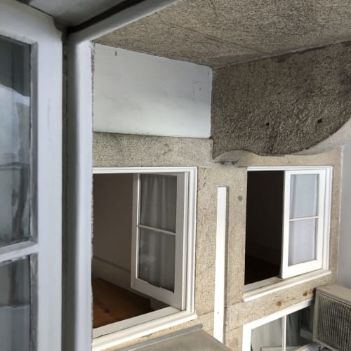 Varanda do apartamento PortoSense em Almada com janelas de moldura branca e paredes de pedra texturizada