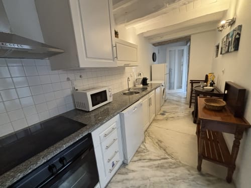 Cozinha moderna tipo corredor no apartamento PortoSense Almada com armários brancos, bancada em granito e acesso à área de jantar