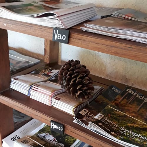 Étagère en bois aux Gravets B&B avec magazines, pomme de pin et sections étiquetées pour activités 'Vélo' et 'Rando'