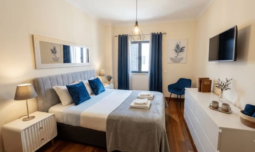 Quarto sereno no To Be Apartments em Lisboa com detalhes azuis, vista para o jardim e móveis modernos