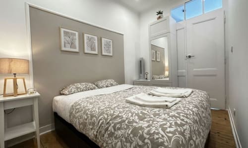 Quarto moderno nos To Be Apartments, Lisboa com roupa de cama estampada, luminária de cabeceira, arte de parede e vista para a cidade