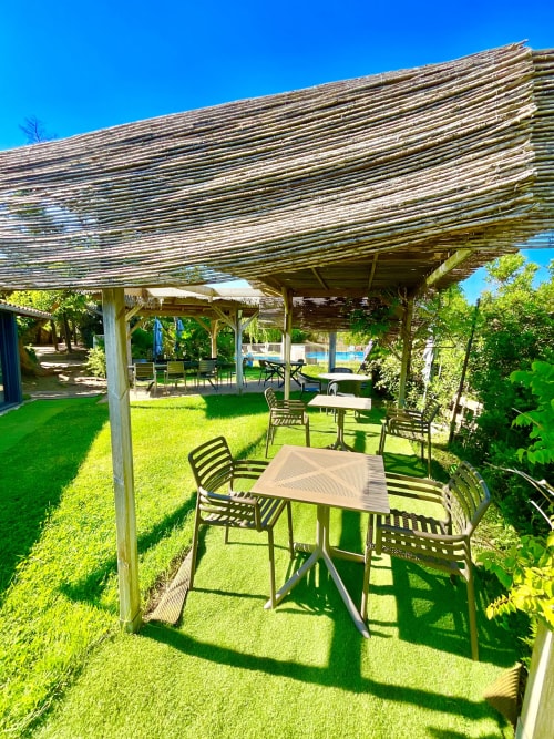 Espace de restauration extérieure au Domaine Pero Longo à Sartène avec pergola, tables, chaises et pelouse verdoyante