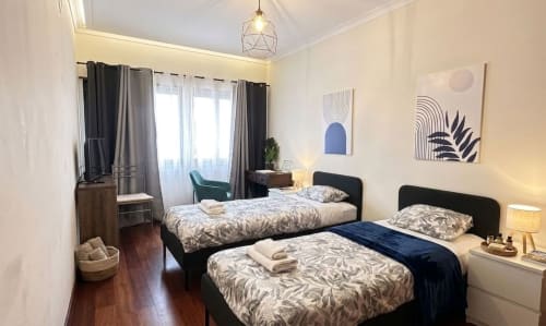 Chambre moderne aux Appartements To be à Lisbonne avec deux lits jumeaux, cadres noirs, literie à motifs, art géométrique mural, suspension