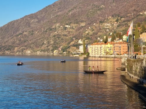 Colorful waterfront buildings and boats on Lake Como in Bellano, Italy with mountain backdrop