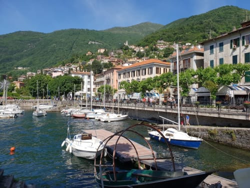 Scenic lakefront harbor in Bellano, Lake Como with moored boats, colorful buildings, and lush green mountains