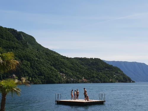 Group enjoying Lake Como from a floating platform with lush green mountains and Villa Vista Lago di Como in Bellano backdrop