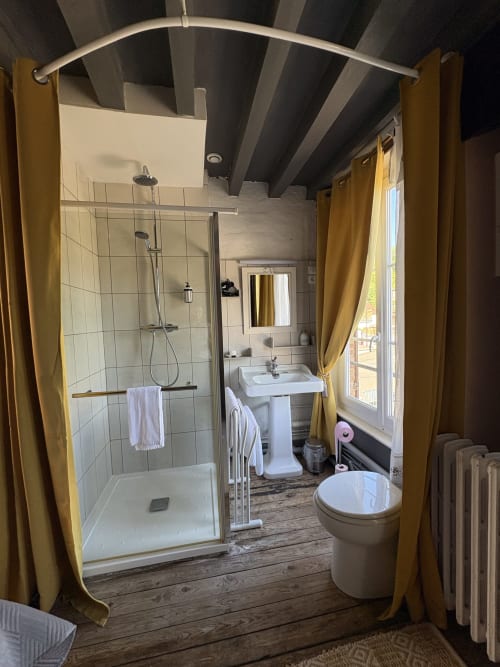 Salle de bains moderne de la Villa Aliénor avec douche à l'italienne, lavabo sur piédestal, toilettes et rideaux dorés encadrant l'entrée