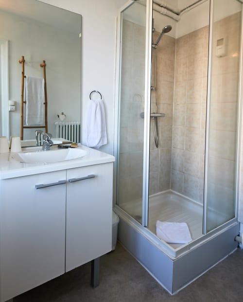 Modern bathroom with white vanity, round sink, large mirror, and glass shower enclosure at La Caravelle hotel in Riom