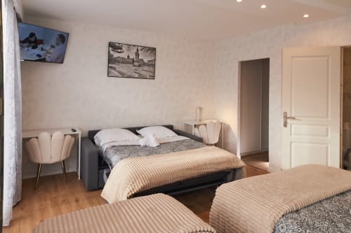 Family bedroom at La Caravelle hotel in Riom with two beds, TV, armchairs, and wooden flooring