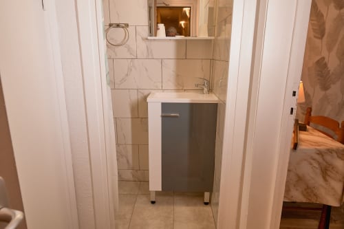 Bathroom vanity with dark cabinet and marble tile backsplash in Chambre Triple at La Caravelle hotel, Riom