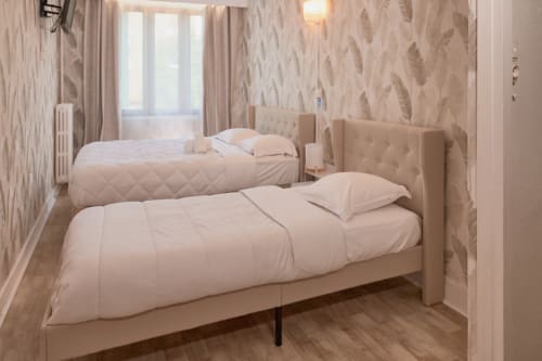 Triple bedroom at La Caravelle hotel in Riom with two beds, beige wallpaper, and wooden flooring