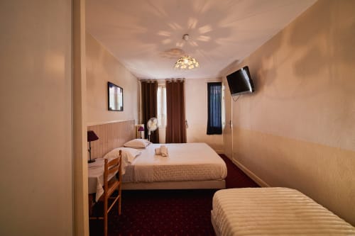 Triple bedroom at La Caravelle hotel in Riom with two beds, flat-screen TV, and warm lighting