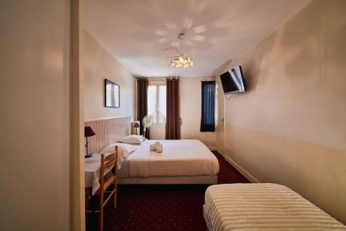 Triple bedroom at La Caravelle hotel in Riom with two beds, flat-screen TV, and warm décor