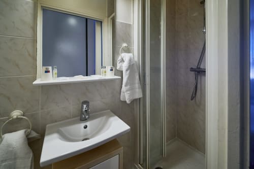 Modern bathroom with white sink, mirror, and shower stall at La Caravelle hotel in Riom, France