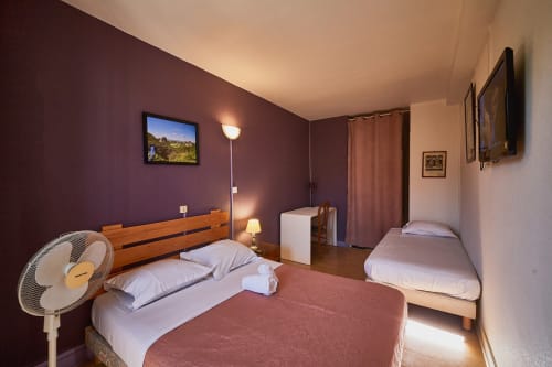 Spacious double bedroom at La Caravelle hotel in Riom with burgundy walls, wooden beds, TV, and modern amenities