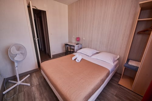 La Caravelle hotel room in Riom with double bed, desk, standing fan, and wooden flooring