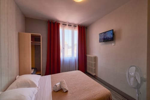 Double bedroom at La Caravelle hotel in Riom with bed, red curtains, TV, and en-suite bathroom
