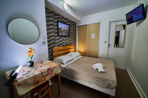 Double Standard room at La Caravelle hotel in Riom with bed, textured headboard wall, round mirror, desk with flowers, and
