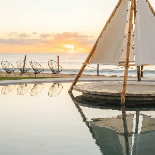 Atardecer en la playa de Vidasoul con velero, tumbonas y piscina infinita reflejando el cielo dorado del resort La Vinorama