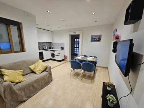 Modern studio apartment at Calm Holiday Homes in Marsa with gray sofa, blue dining table, kitchenette, and wall-mounted TV