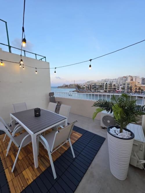 Rooftop terrace at Calm Holiday Homes in Marsa with dining table, pendant lights, and Mediterranean Sea views at sunset.