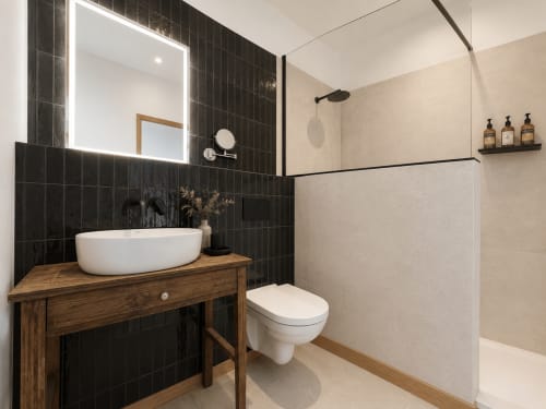 Modern bathroom at Le Palmier Aigues-Mortes with black tile walls, white basin sink, toilet, and walk-in shower