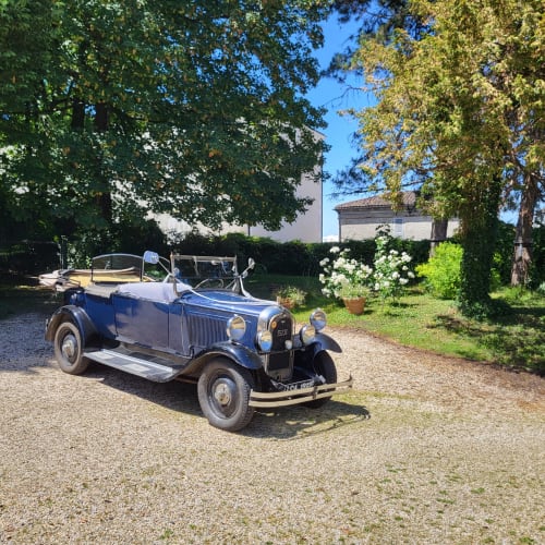 Voiture décapotable bleu vintage au Logis des Tourelles, gîte en Cognac, France, avec jardins et bâtisse en pierre.