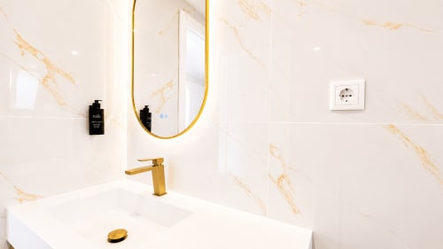 Banheiro de luxo moderno na Quinta das Susandas com paredes em mármore, acabamentos em dourado, espelho redondo e pia em branco