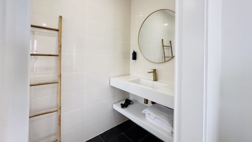 Banheiro moderno com azulejos brancos, espelho redondo dourado, escada de madeira para toalhas e lavatório branco no hotel Quinta das Susandas