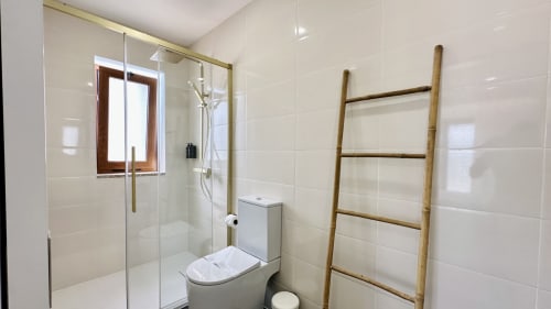 Banheiro moderno com chuveiro walk-in, azulejos brancos e escada de madeira no hotel Quinta das Susandas em Tresouras