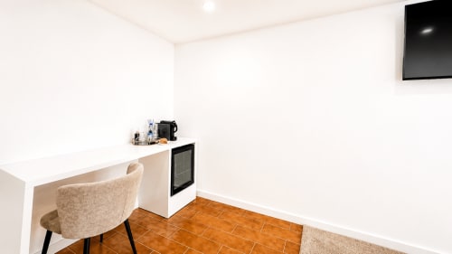 Escritório moderno com cadeira bege, frigobar e TV no quarto de luxo da Quinta das Susandas, Portugal