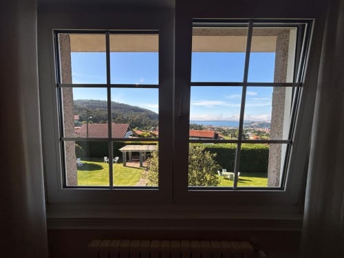 Vista desde ventana de habitación de casa privada en Baiona con jardín, montañas, mar y tejadillos rojo