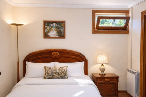 Dormitorio elegante con cama de madera, ropa de cama blanca, ventana con vistas al mar y decoración tradicional 