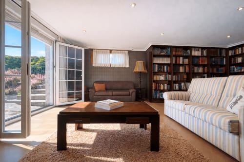 Espacioso salón de la casa Mar y Sol en Baiona con vistas al mar, estanterías de madera oscura, sillón a rayas y acceso a terraza