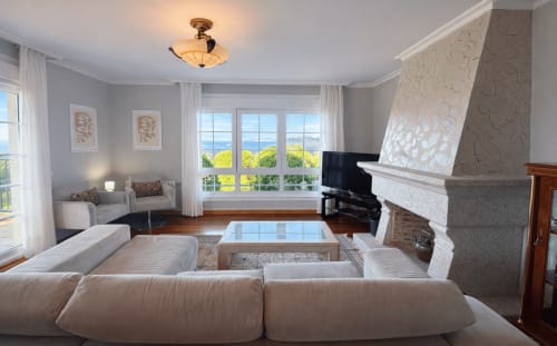 Elegante sala de estar en casa Mar y Sol, Baiona con vistas al mar, chimenea, piano y paisaje costero desde las ventanas