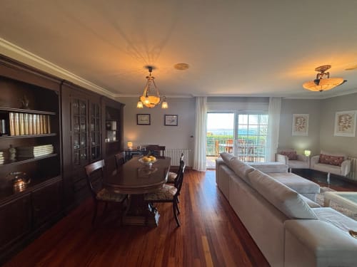 Elegante sala de estar diáfana en la casa Mar y Sol, Baiona, con vistas al mar, muebles de madera oscura, chimenea y estilo moderno