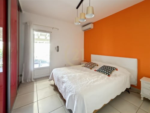Chambre lumineuse avec mur d'accent orange, lit blanc, suspensions en bois et vue sur le jardin à Villa Sant Ambroggio