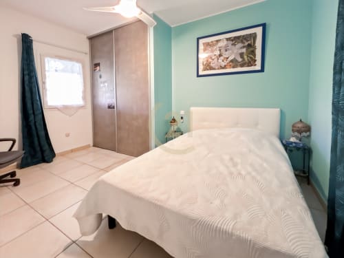 Chambre lumineuse de villa à L'Île-Rousse avec murs turquoise, lit blanc, armoire et vue sur jardin