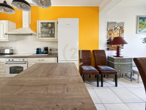 Cuisine et séjour de villa moderne avec mur d'accent jaune vif, appareils électroménagers blancs, chaises en cuir marron et espace repas