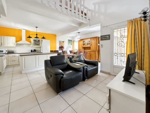 Espace de vie d'une villa familiale aux accents jaunes, fauteuils noirs, cuisine et vue sur le jardin à L'Île-Rousse