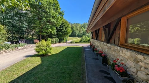 Les Grands Champs B&B à Attignat-Oncin : bâtisse en pierre moderne avec pelouse paysagée, fleurs et vue sur les montagnes