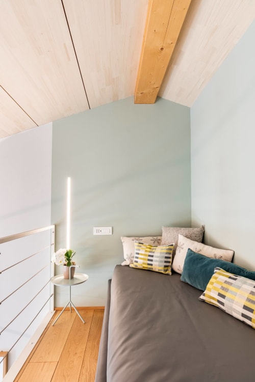 Camera luminosa e minimalista con travi in legno, pareti verde salvia, letto matrimoniale con cuscini decorativi, pavimenti in legno
